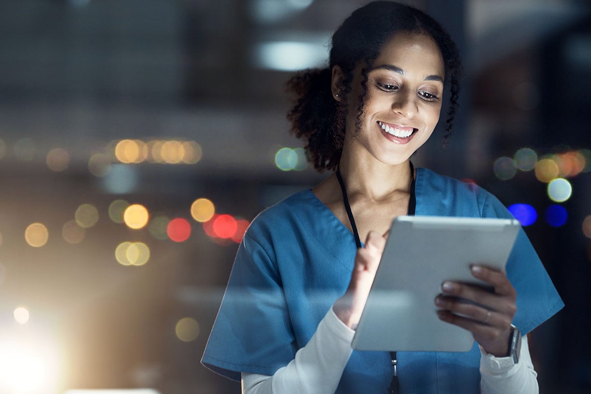 nurse smiling while using a tablet in a dimly lit room